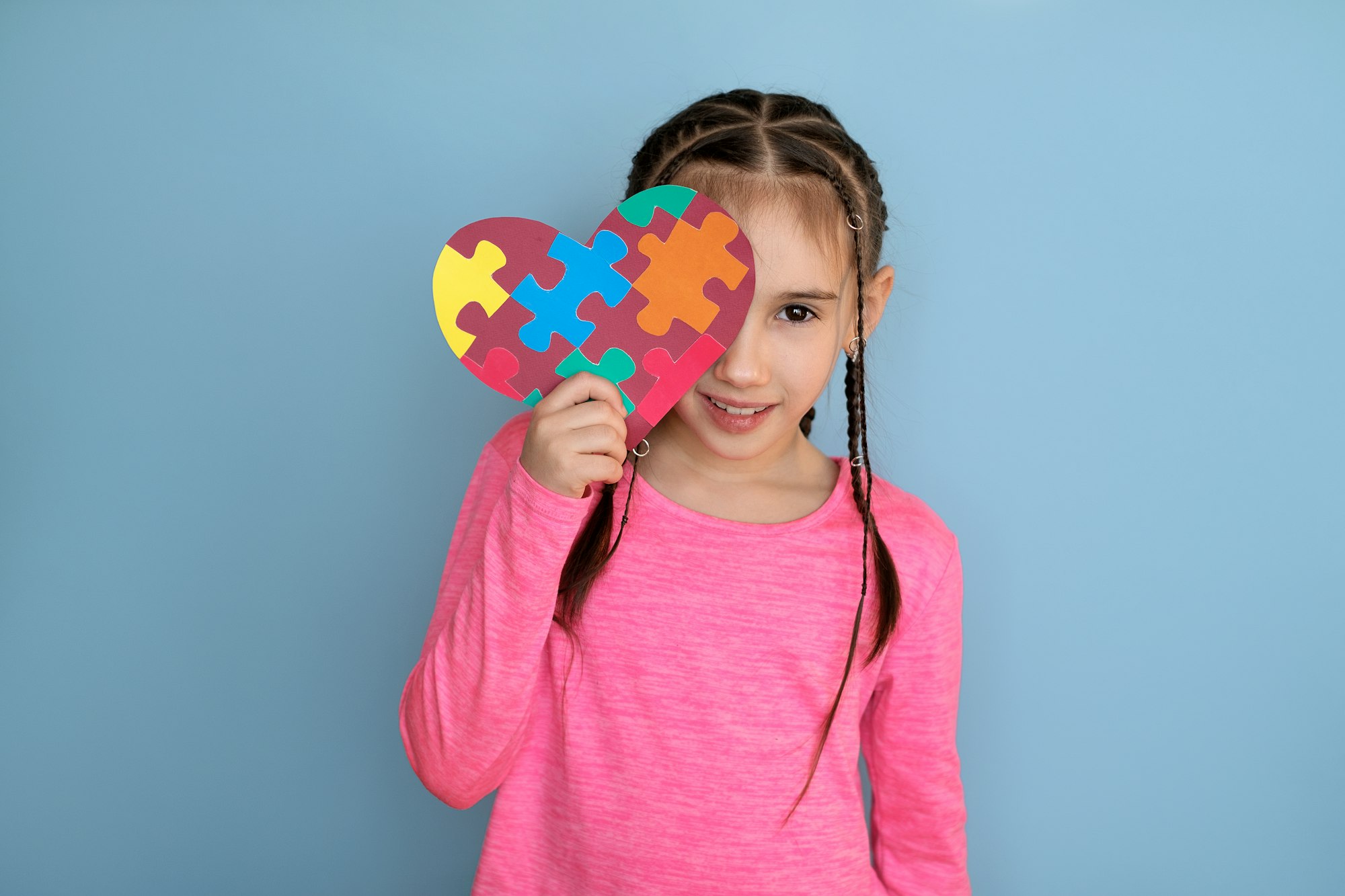 Stylish girl gently holds heart-shaped card with puzzles, covering part of face